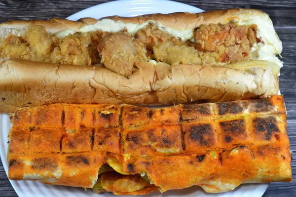 Baharatlı çıtır tavuklu çeşitli sandviçler, patates kızartması, mayonez ve lahana salatası uzun bir çörek ve Casta tavuğu, salatalık turşusu ve patates dilimleri, tortilla ekmeğiyle sarılmış.