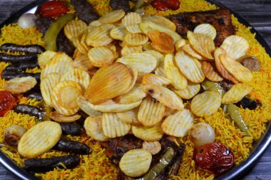 Bir tepsi çeşit çeşit ızgara kömür ızgara ızgara biftek kıymalı et kufta, sosis, ızgara tavuk, kızarmış patates cipsi, yeşil biber, domates, soğan ve sarı Hint Basmati pilavı.