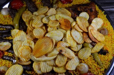 Bir tepsi çeşit çeşit ızgara kömür ızgara ızgara biftek kıymalı et kufta, sosis, ızgara tavuk, kızarmış patates cipsi, yeşil biber, domates, soğan ve sarı Hint Basmati pilavı.