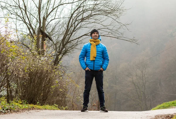 Stock image Man walking in mountain in autumn, winter time, observing nature in national park. Male wears warm casual clothes, blue jacket, hat, yellow scarf ,jeans Horizontal. Leafless trees. Haigh quality photo