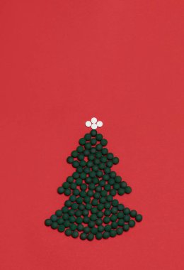 Kırmızı arka plan, ilaç maketi, yeşil beyaz haplardan, haplardan, vitaminlerden yapılmış Noel ağacı. Mutlu Noeller, mutlu yıllar, eczane kartpostalı, düz, üst görünüm, dikey kopyalama alanı