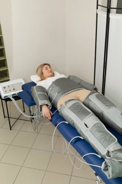 Basınç terapisi prosedürü. Spa kliniğinde masaj kıyafeti giymiş bir kadın varisli damarların tedavisi, ödem, lenfatik drenaj, kilo kaybı. Rahatlama ve tedavi. Basınç terapisi. Dikey, kopyalanmış boşluk