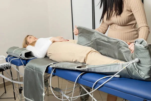 Pregnant business woman runs, manages own business, spa salon, prepares pressure therapy procedure, massaging suit for client. Pressotherapy. Maternal entrepreneurship, work, sustainability Horizontal