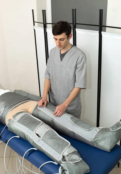 Erkek uzman, spa salonundaki kadın müşteriye masaj kıyafeti giydirerek baskı terapisi prosedürünü yönetiyor. Basınç terapisi, lenfatik drenaj masajı. Dikey düzlem