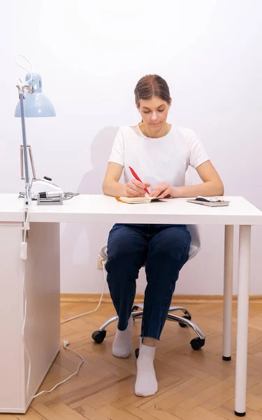 Nail beautician makes notes in notebook with pen, sitting at workstation, table in nail beauty treatment salon. Professional tools are on white table. Manicurists routine. Vertical plane