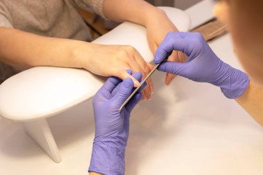 Manikür mater dosyaları güzel kadınların tırnakları, el ele tutuşmalar. Beyaz manikür ustası, spa salonundaki beyaz iş istasyonunda eldivenlerle çalışıyor. Yumuşak, güvenli güzellik tırnak bakımı, tedavi. Yatay