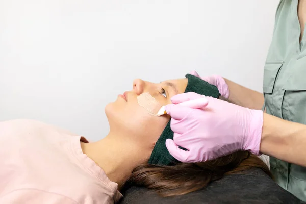 Acne treatment. Cosmetologist does cleaning skin mask procedure on female teens face. Teenage girl lying on medical couch. Dermatologist in pink gloves applies special gel,cream by brush. Horizontal