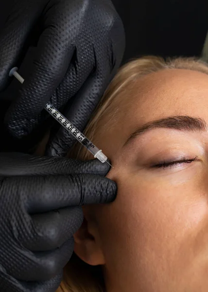 stock image Closeup of Caucasian woman gets botox cosmetic injection in eye area. Beauty physician inserts needle of syringe into face of beautiful female. Cosmetologist, aesthetic medicine. Vertical plane