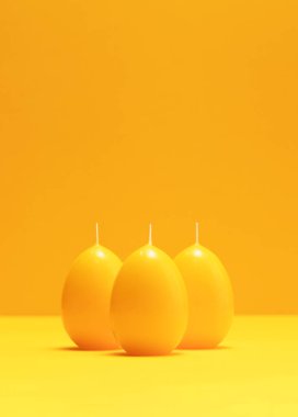 Tek renkli turuncu arka planda yumurta şeklindeki sarı turuncu mumlar. Minimalist Mutlu Paskalyalar konsepti. Yaratıcı çevreci Paskalya tebrik kartı, metin için kopyalama alanı. Dikey düzlem.