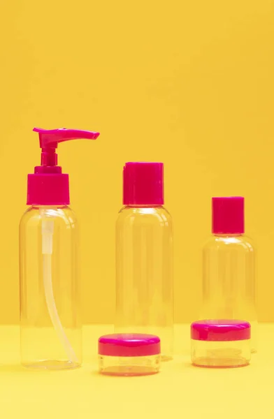 Closeup fuchsia travel bottle kit for liquids, cream. Toiletries Beauty Kit on yellow orange background. Airplane approved luggage reusable container size. Summer time, vacation concept. Vertical.