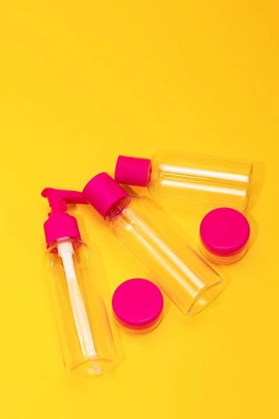 Top view travel bottle kit for liquids, cream. Toiletries Beauty Kit on yellow orange background. Airplane approved luggage reusable container size. Summer time, vacation. Vertical. Copy space.