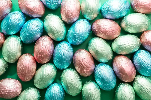 Background, texture closeup small Easter chocolate eggs, sweets wrapped in colorful bright foil green blue background. Religious Happy Easter concept, holiday. horizontal plane