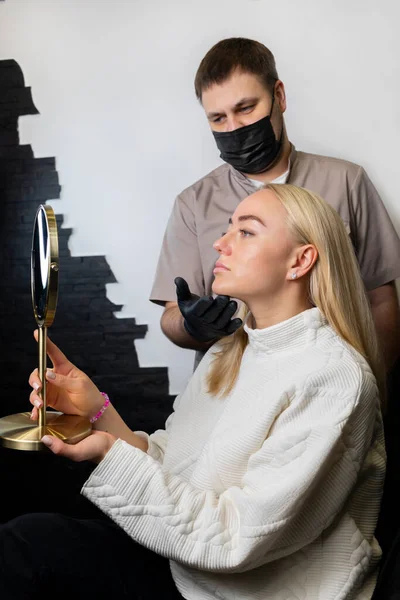男医生 美容师演示女性注射美容术的效果 用填充物整容 白人高兴地看着镜子 美容师美容师垂直平面 — 图库照片