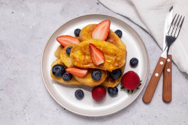 Düz Torrijas, dilimlenmiş Brioche 'den yapılmış yumurtalı ekmek, üzerine portakal sosu, jöle, taze yaban mersini, tabakta çilek, çatallı granit masa, bıçakla servis edilmiş. Kahvaltıda tatlı. Yatay..
