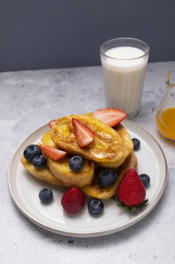 Torrijas, dilimlenmiş Brioche, Ekmek, Portakal şurubu, taze yabanmersini, Tabakta çilek, Granit Masada bir bardak süt. Kahvaltıda tatlı. Dikey düzlem.