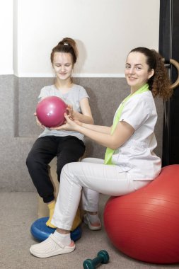 Gülümseyen çocuk, engelli genç kız fizik tedavi uzmanı ve rehabilitasyon uzmanının desteğiyle fiziksel egzersiz yapıyor. Rehabilitasyon. Kas iskeleti bozukluğu. Dikey düzlem.