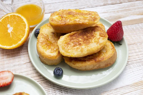 stock image Torrijas, Spanish Style French Toast Served With Orange Topping, Glaze, Fresh Blueberries, Strawberry On Green Plate, Wooden Table. A Half Of Orange. Spanish Dessert. Horizontal plane.