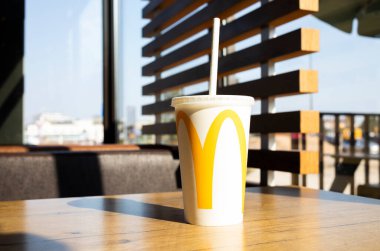 McDonald 'ı tazeleyen büyük beyaz bardakta milkshake, logolu kağıt kamış restoranda, McCafe' de. Güneşin Sert Gölgeleri. Yaz içeceği. Polonya, Bialystok 25 Nisan 2023 Yatay Uçak.