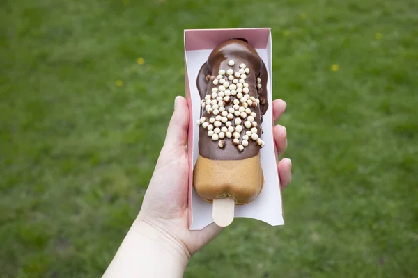 Festival Street Food Penis Shaped Waffle On Wooden Stick With Dark Chocolate, Decorated With White Air Corn Balls In Paper Box In Human Hand Outdoor. Sweet Cookie Horizontal Plane.