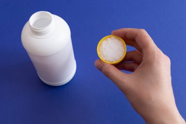 Kadın El Tutuşu Boru Temizleyici Granülleri. Lavabodaki tıkanıklığın kaldırılması, kimyasal ilaçlarla yıkanması. Mutfak ve banyodaki klozeti temizliyorum. Arkaplanda Beyaz Plastik Şişe.