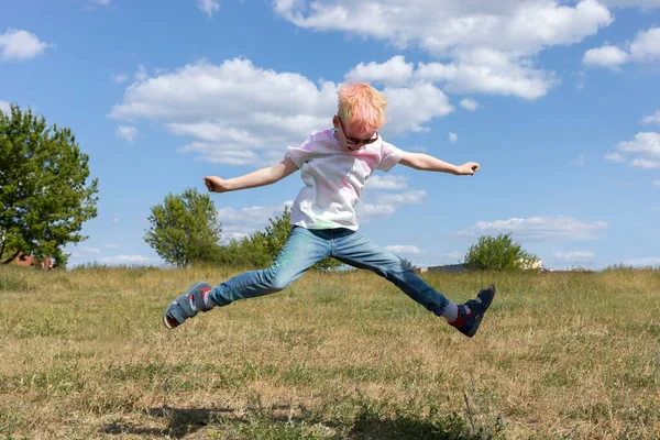 Renkli boyalı küçük sarışın çocuk, elbiseli pudra Holi Renk Festivali 'nde havaya zıplıyor. Duygusal Mutlu Çocuk. Mavi Gök, Arkaplanda Yeşil Ağaçlar, Yaz. Yatay düzlem. Yüksek kalite fotoğraf