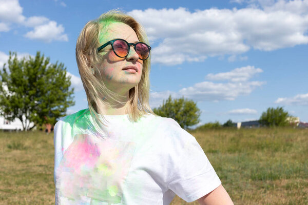 Portrait Beautiful White Blond Woman With Colored Dye, Powder On Face And Cloth On Holi Colors Festival In Meadow, Sunny Day. Playful Cultural Event With Throwing Bright Neon Powder. Horizontal Plane.
