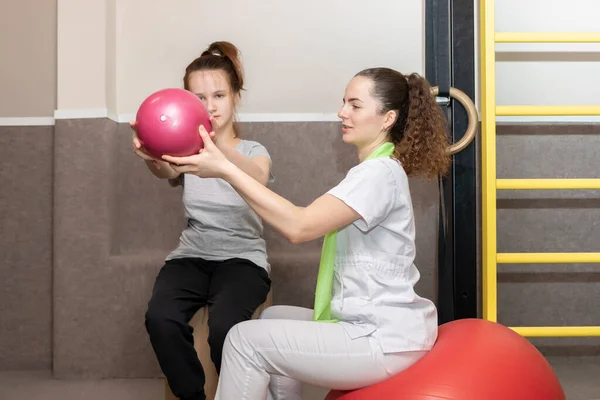 Gülümseyen kız, engelli çocuk rehabilitasyon uzmanı, spor salonundaki fizyoterapist eşliğinde topla fiziksel egzersiz yapıyor. Rehabilitasyon. Yatay düzlem. Yüksek kalite fotoğraf