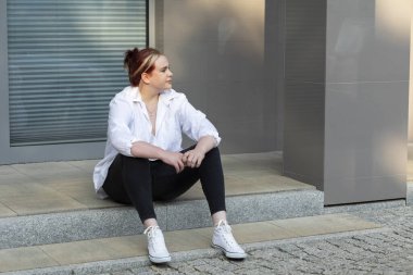 Güzel, gülen stil artı 20 beden kadın, Zoomer yaz günü beton sokak merdivenlerinde oturur, uzaklara bakar. Genç Kafkasyalı Öğrenci eğleniyor. Şehir Yaşam Tarzı. Yatay Düzlem.