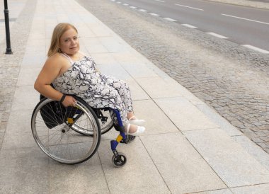 Tekerlekli sandalyede kısa duruşu olan, gülümseyen güzel bir kadın yaz gününde otobüs durağında toplu taşıma için bekliyor. Engelli Yetişkin Kadın 'ı. Metin için Boşluğu Kopyala. Yatay Düzlem.