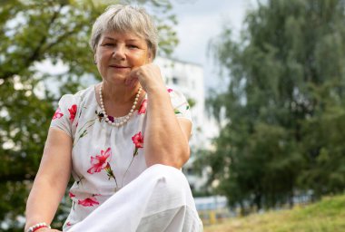 Çayır 'da oturmuş gülümseyen ve rahatlatan güzel beyaz kadın portresi. Emeklilik ve özgürlük. Avrupa tarzı, olgun, orta yaşlı bir kadın. Yatay düzlem, uzayı kopyala. Yüksek kalite fotoğraf