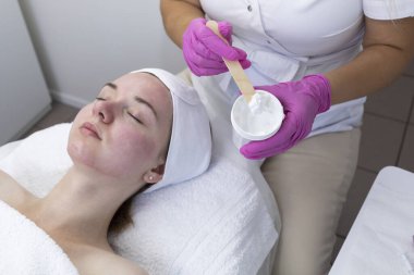 Kırpılmış Kozmetolog, Güzellik Uzmanı Nemlendirici Maske Uygulayan, Güzellik Salonunda Kimyasal Soyulduktan sonra Kadınlar İçin Krem Süren Kızıl Cilt. Kozmetik ve Yüz Bakımı. Yüz bakımı. Yatay Düzlem.