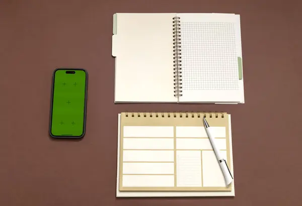 Top View Mockup Office Desk With Blank Notebook, Weekly Paper Planner And Chroma Key Screen of Smartphone, Pen On Brown Background. Horizontal Plane Minimal Flat Lay Style. Template. Horizontal Plane
