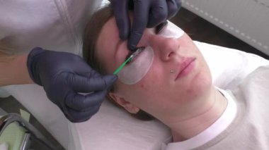 Kirpikçi, Güzellik Salonu 'nda kirpik arıtma prosedürü için kirpiklerin kirpiklerine serum uygular. Kıvırcık, lekeli, Kırbaç için uzatma prosedürleri. Yatay olarak. Adım adım. Yavaş Hareket