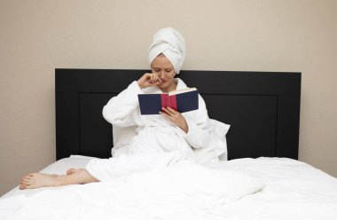 30 'larında bir kadın yatakta oturup kitap okurken ağlıyor. Duygusal Empati Yüz İfadesi. Duyarlı Kafkas Olgun Kadın Romantizm Okuyor, Romantik Aşk Üzücü Hikayesi. Kitap Aşığı, Yatay Düzlem.