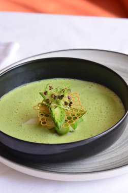 Kremalı yeşil çorba, beyaz arka plan, siyah kasede servis ediliyor.