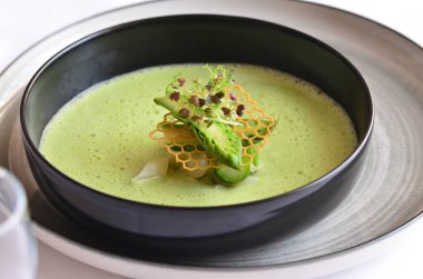 Kremalı yeşil çorba, beyaz arka plan, siyah kasede servis ediliyor.