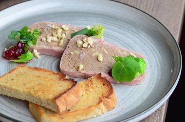 Domuz eti ezmesi, badem, domuz pastırması, kızarmış ekmek, bir restoranda ahşap bir masada servis ediliyor.