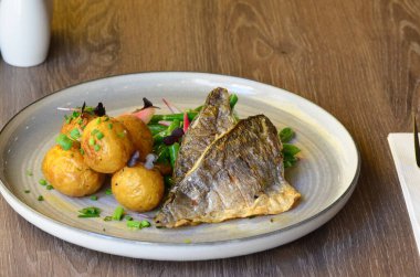 Fasulyeli balık filetosu, patates, yemeğin arkasında servis edilir.