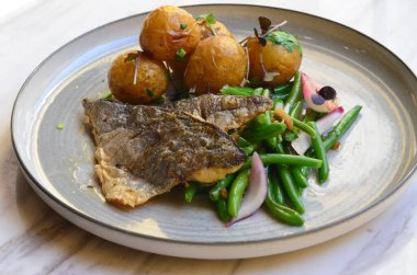 Fasulyeli balık filetosu, patates, yemeğin arkasında servis edilir.