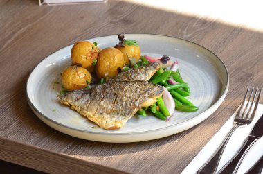 Beyaz tabakta patates ve sebzeli kızarmış balık.