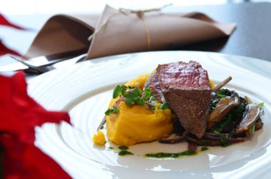 Orta pişmiş biftek, restoran arka planı, beyaz tabakta servis edilmiş, yanında meze ile dilimlenmiş pembe biftek.