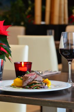 Orta pişmiş biftek, restoran arka planı, beyaz tabakta servis edilmiş, yanında meze ile dilimlenmiş pembe biftek.