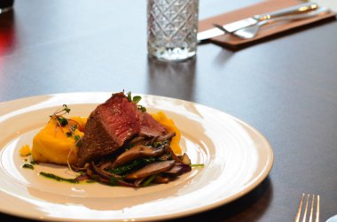 Biftek, beyaz tabakta patates ve mantarla servis edilir.