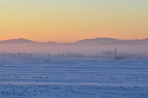 Foggy winter landscape with church and village in the background.