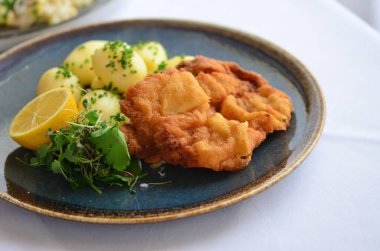 Kızarmış balık fileto, patates ve sebzeli beyaz tabak.