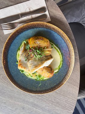 Sebzeli balık filetosu ve beyaz tabakta otlar.