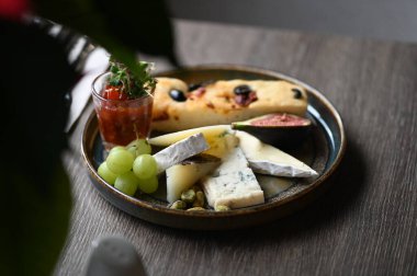 Peynir tabağında çeşitli peynirler, üzümler, incirler ve üzümler var..