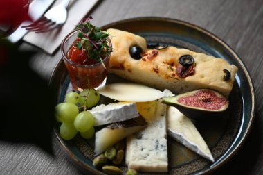 Peynir tabağında çeşitli peynirler, üzümler, incirler ve üzümler var..