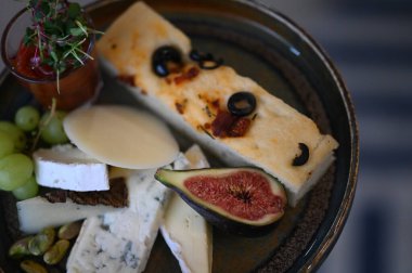 Peynir tabağında çeşitli peynirler, üzümler, incirler ve üzümler var..