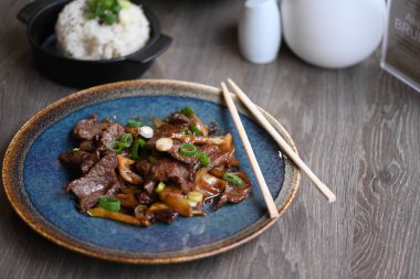 Kızarmış pirinç, domuz eti ve Kore usulü sebzeli siyah tabakta. Kore yemekleri..